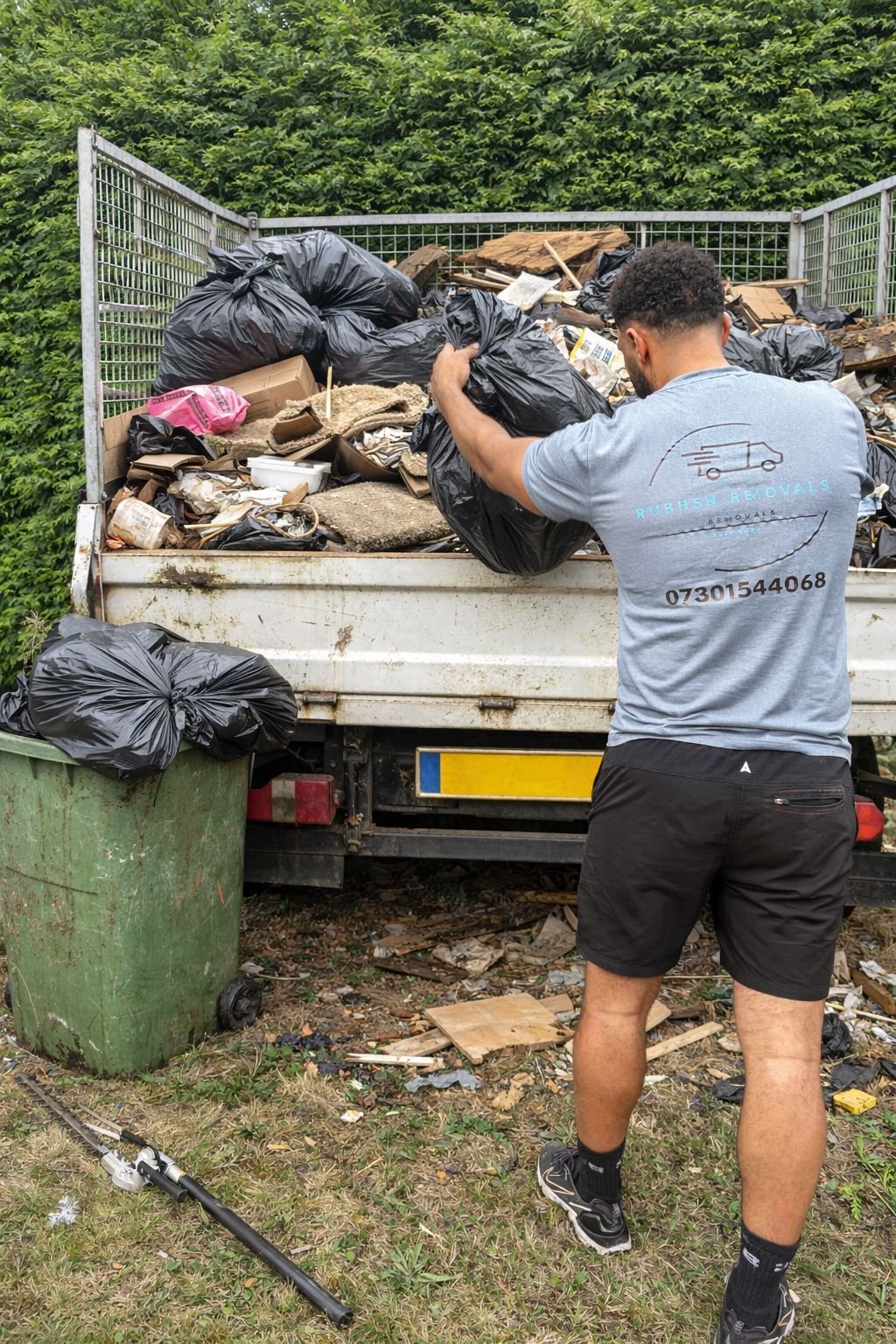 A Litter Me Removals team member in branded uniform loading a bagged waste into a full caged tipper truck