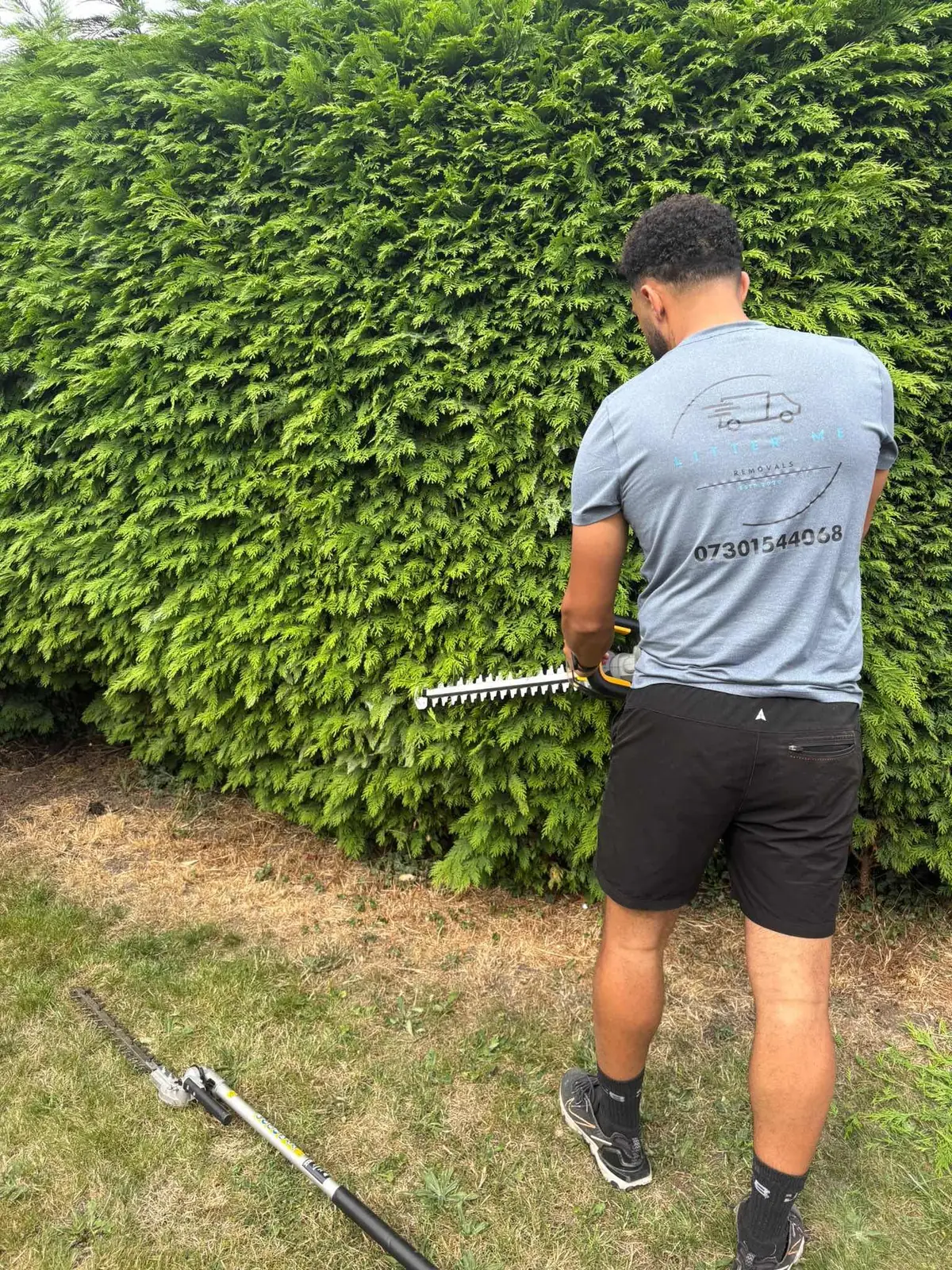 Litter Me Removals team member in branded uniform trimming a large garden hedge